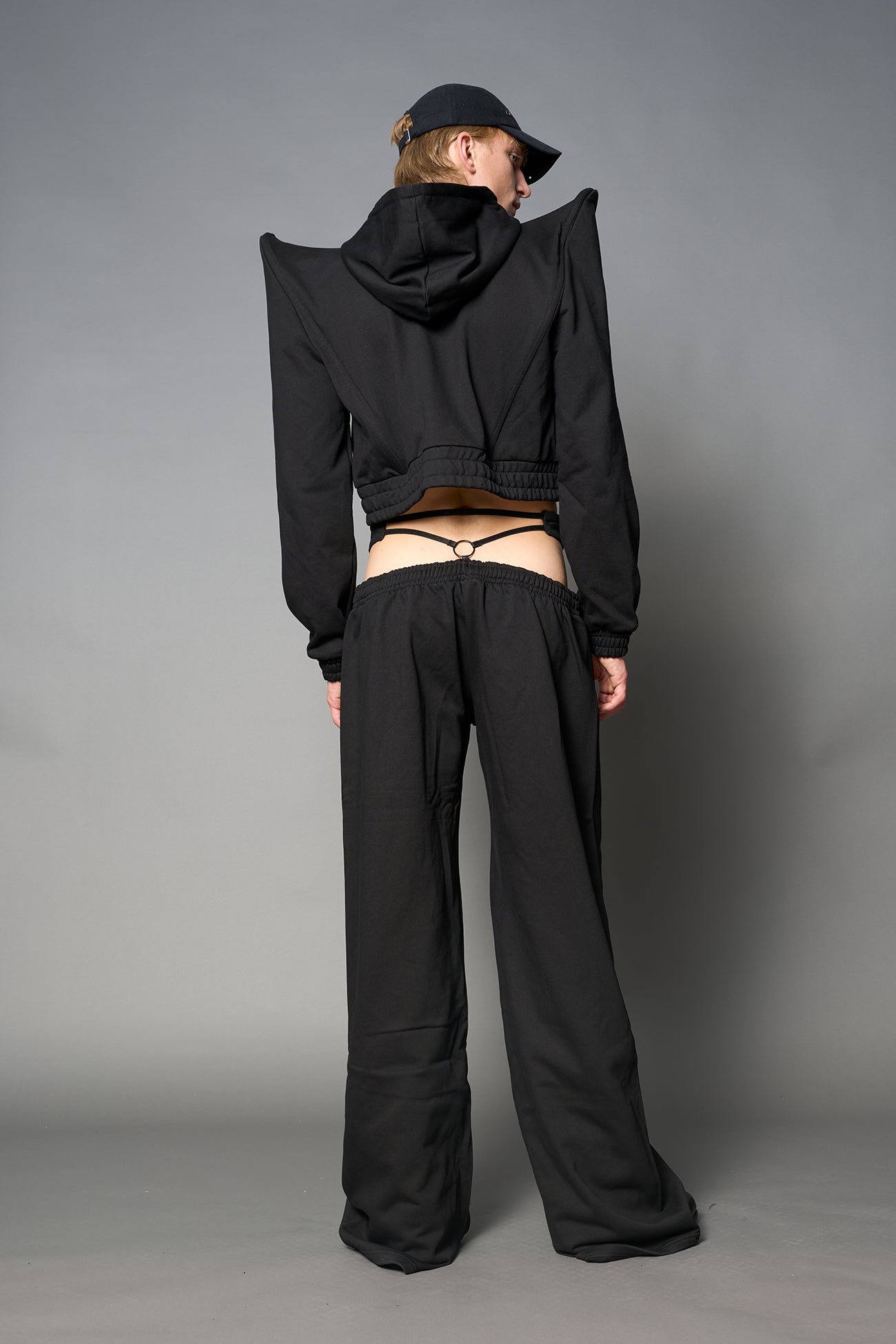 Model wearing a black cropped hoodie with exaggerated spike shoulders, drawstring hood