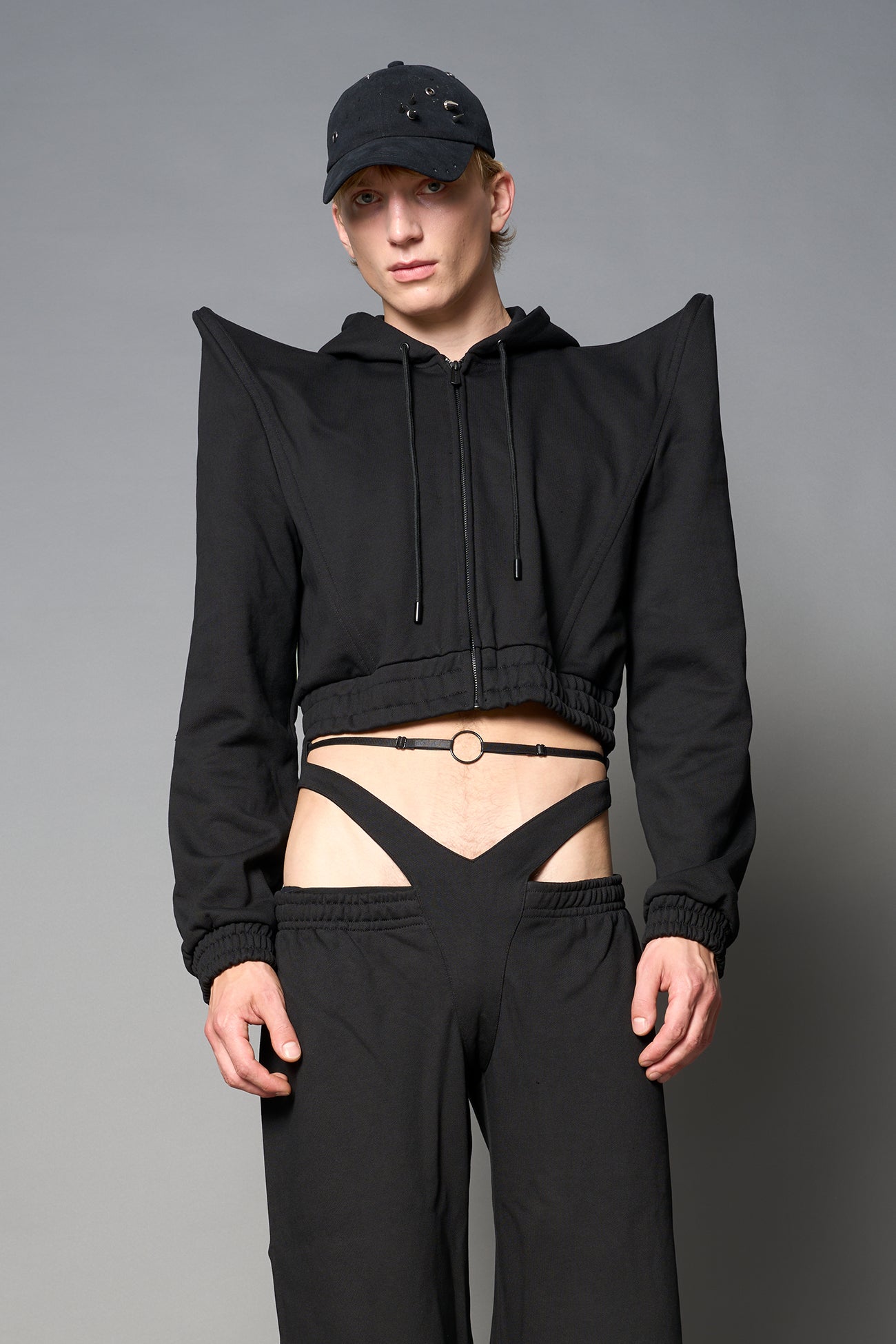 Model wearing a black cropped hoodie with exaggerated spike shoulders, drawstring hood