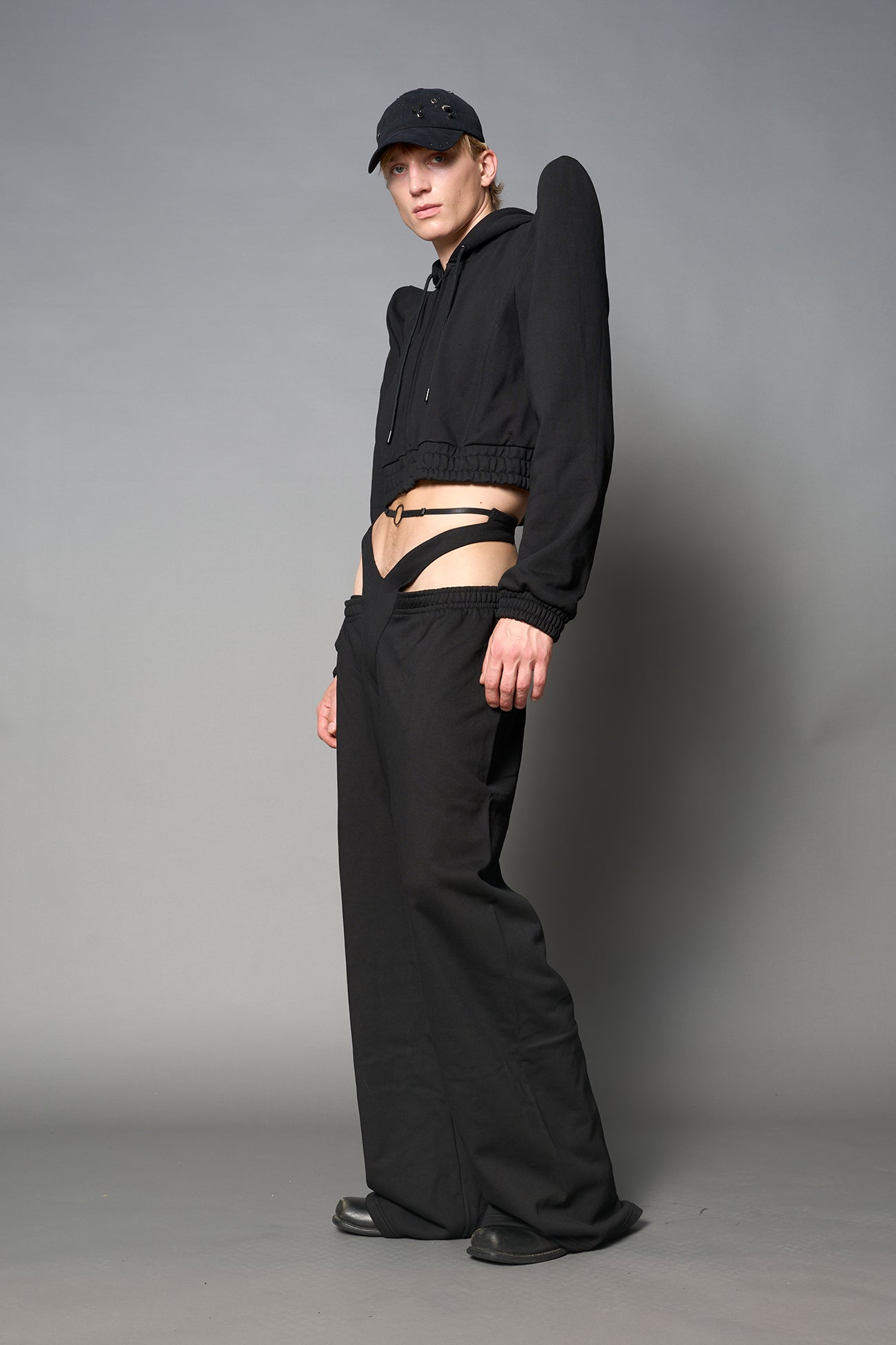 Model wearing a black cropped hoodie with exaggerated spike shoulders, drawstring hood