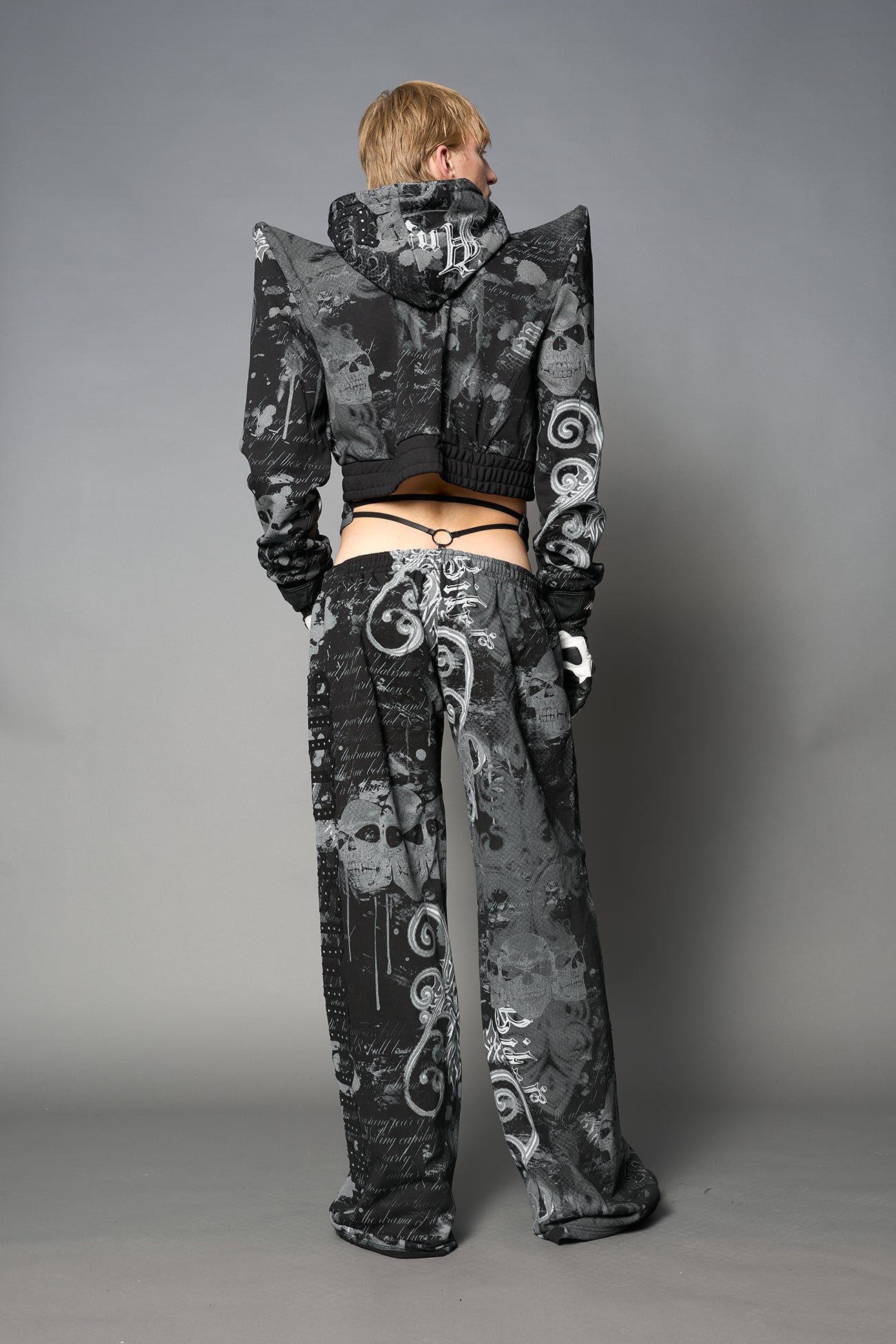 Model wearing a black print cropped hoodie with exaggerated spike shoulders, drawstring hood