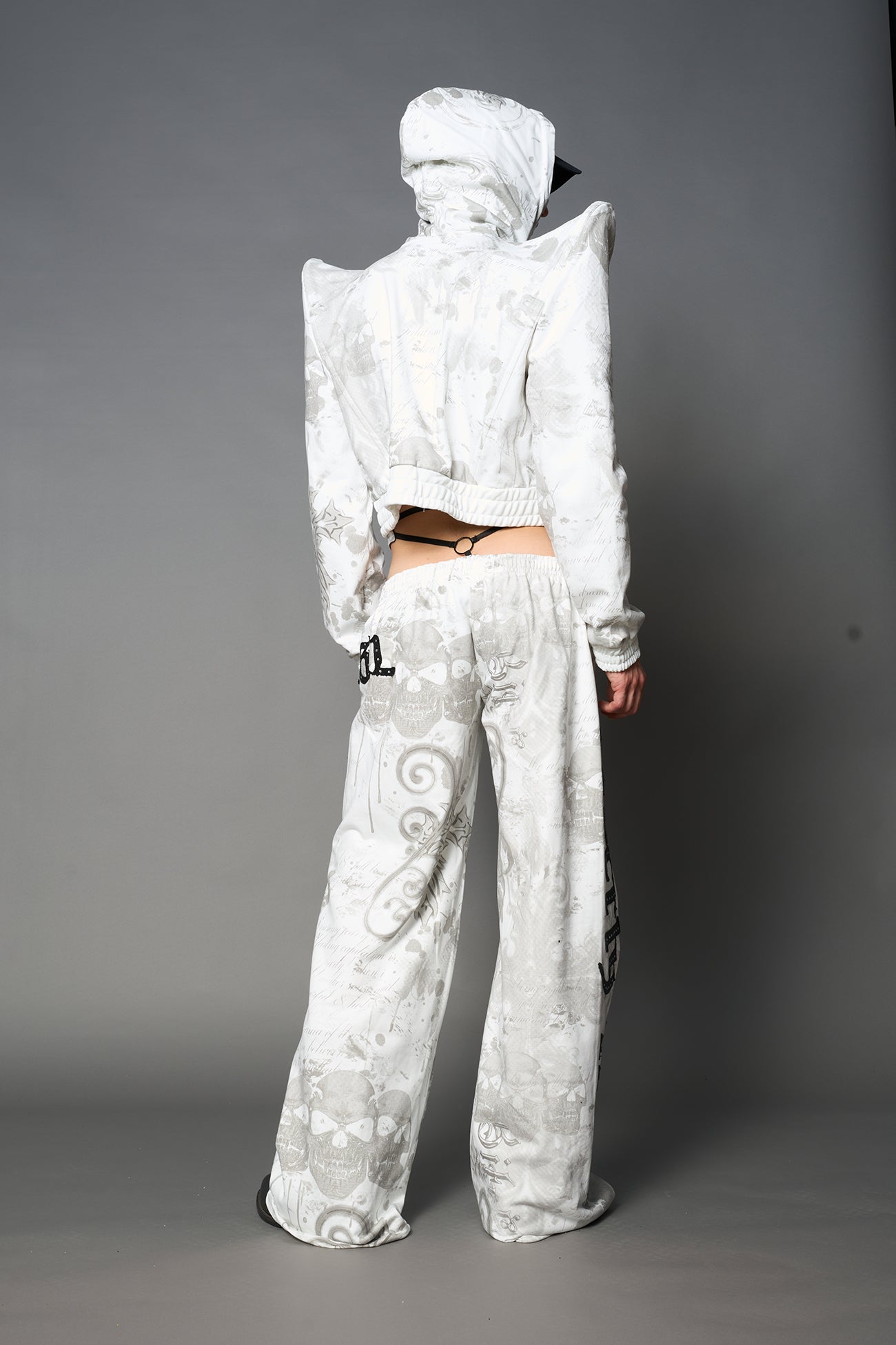 Model wearing a white print cropped hoodie with exaggerated spike shoulders, drawstring hood