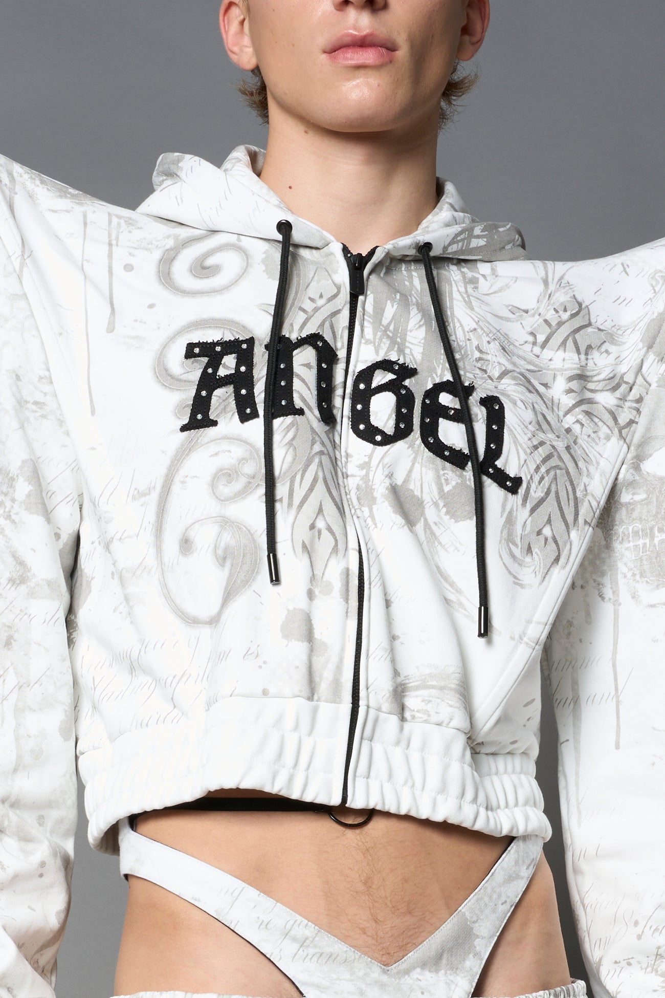 Model wearing a white print cropped hoodie with exaggerated spike shoulders, drawstring hood