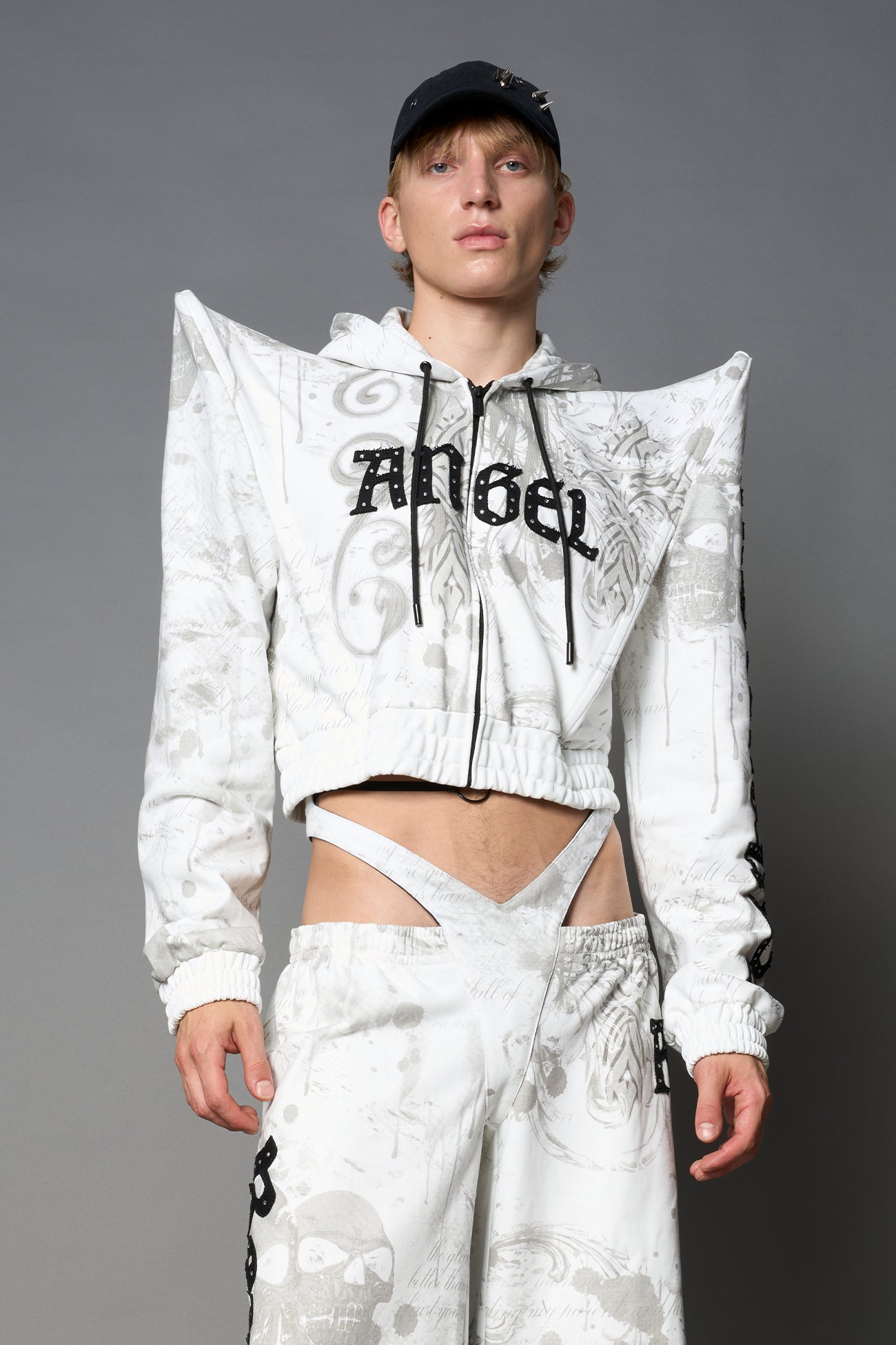 Model wearing a white print cropped hoodie with exaggerated spike shoulders, drawstring hood