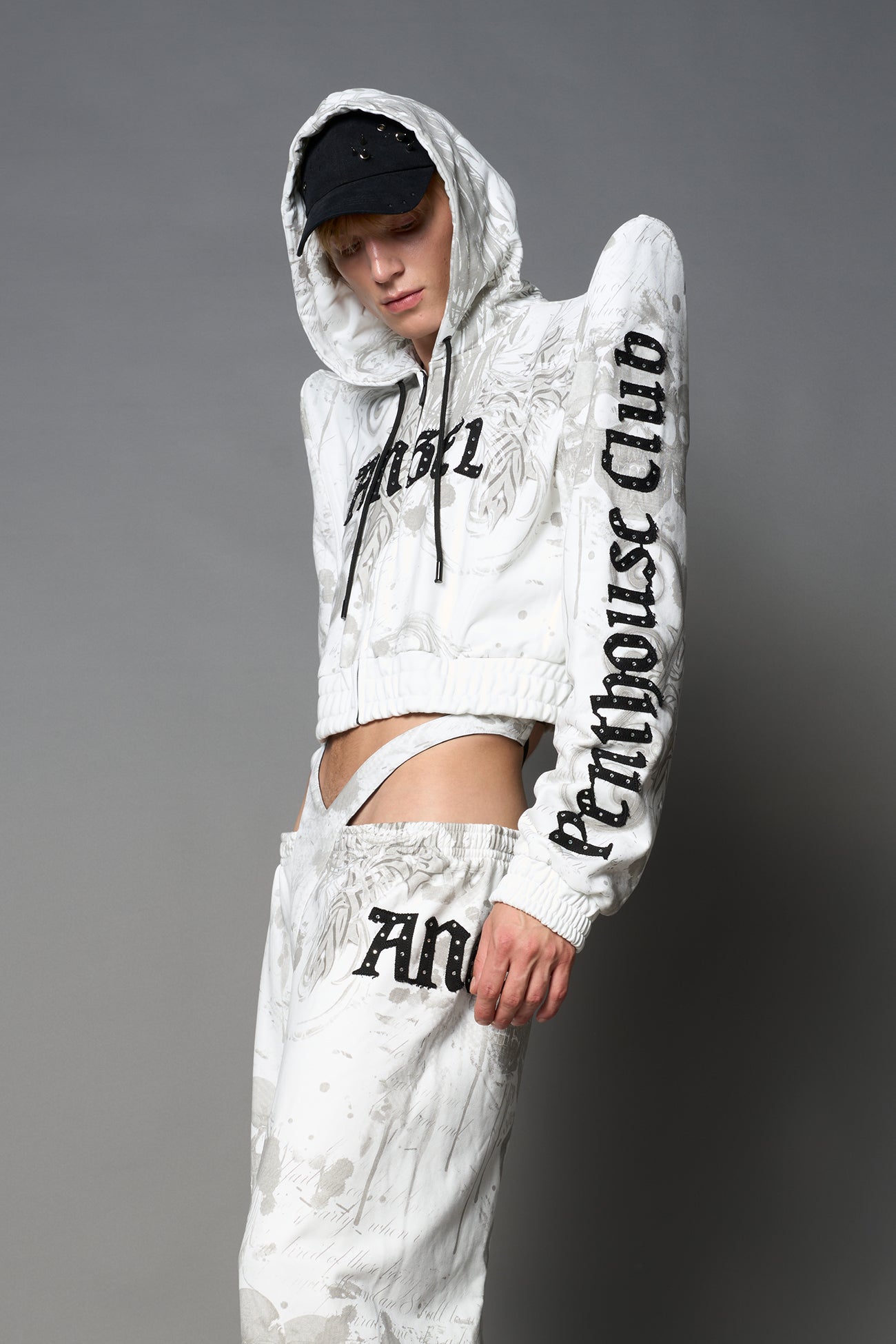 Model wearing a white print cropped hoodie with exaggerated spike shoulders, drawstring hood