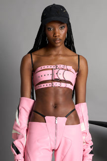 pink vegan leather belt top with three adjustable grommet straps, oversized metal buckles, and circular hardware – edgy bondage-inspired crop top for festival or clubwear.

