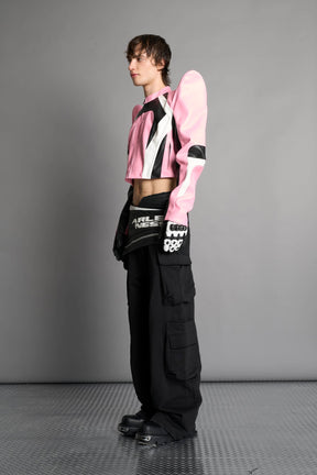 Model wears the pink Namilia Spike Moto Jacket with wire shoulder pads, branded zipper, band collar, zippered breast and waist pockets, motocross-style lines, and black logo rubber tag on the back.