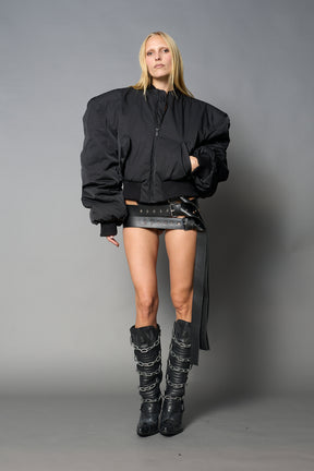 model wears black oversize cropped nylon bomber with exaggerated shoulderpads and ruching on sleeves.