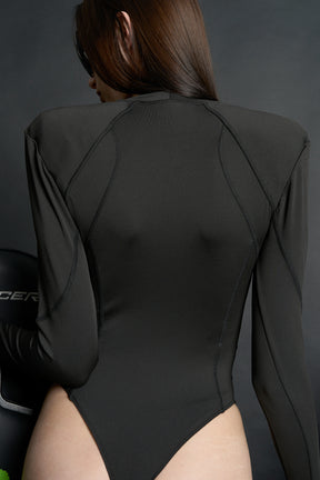 Model wears a long-sleeved black lycra stretch bodysuit with string back and detachable padded shoulders, rhinestoned slogan, thumbhole gloves.
