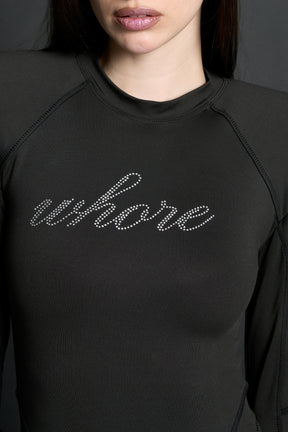 Model wears a long-sleeved black lycra stretch bodysuit with string back and detachable padded shoulders, rhinestoned slogan, thumbhole gloves.