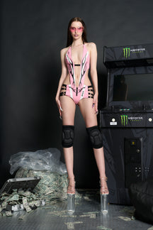 Model wears a pink panelled vegan leather bodysuit with deep V neckline, open back, flame stitching, and slogan embroidery.