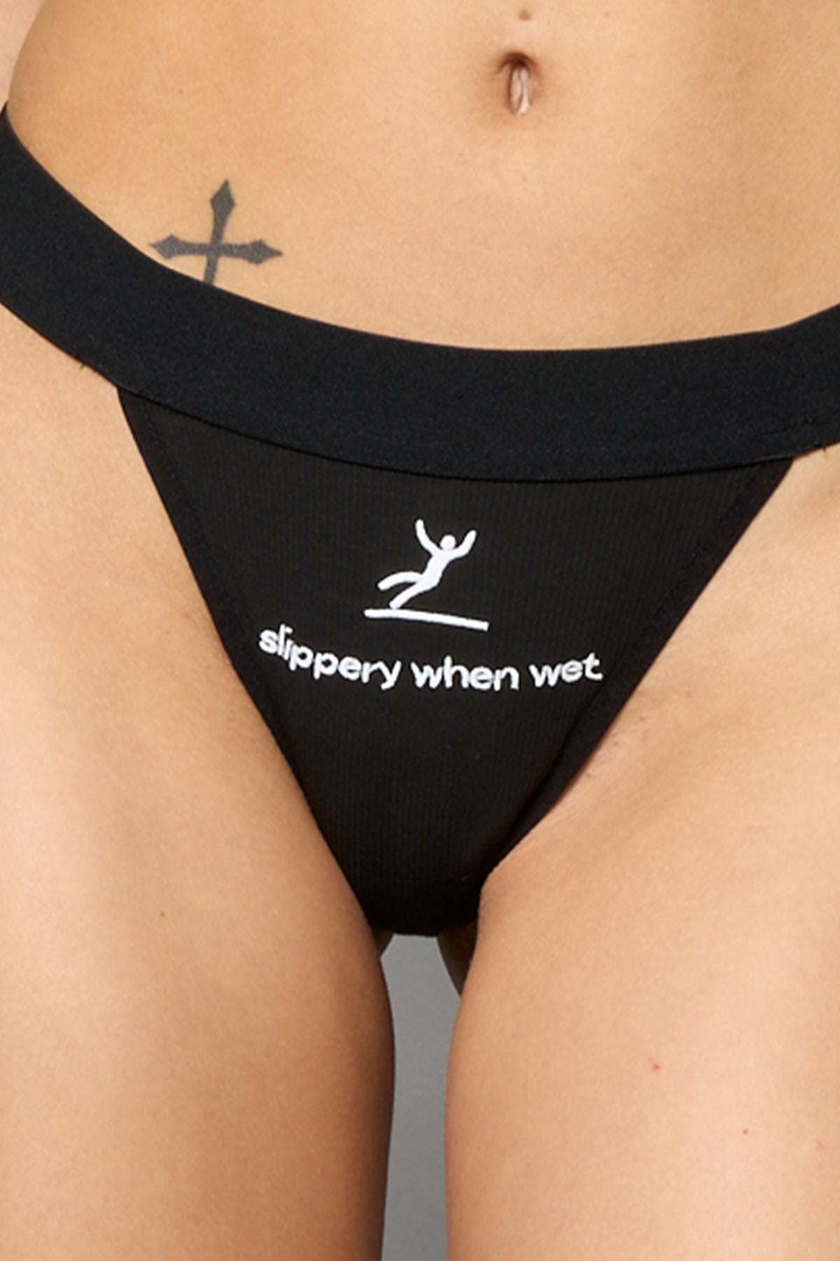 Black Namilia thong with white ‘slippery when wet’ graphic print on front, ribbed elastic waistband.