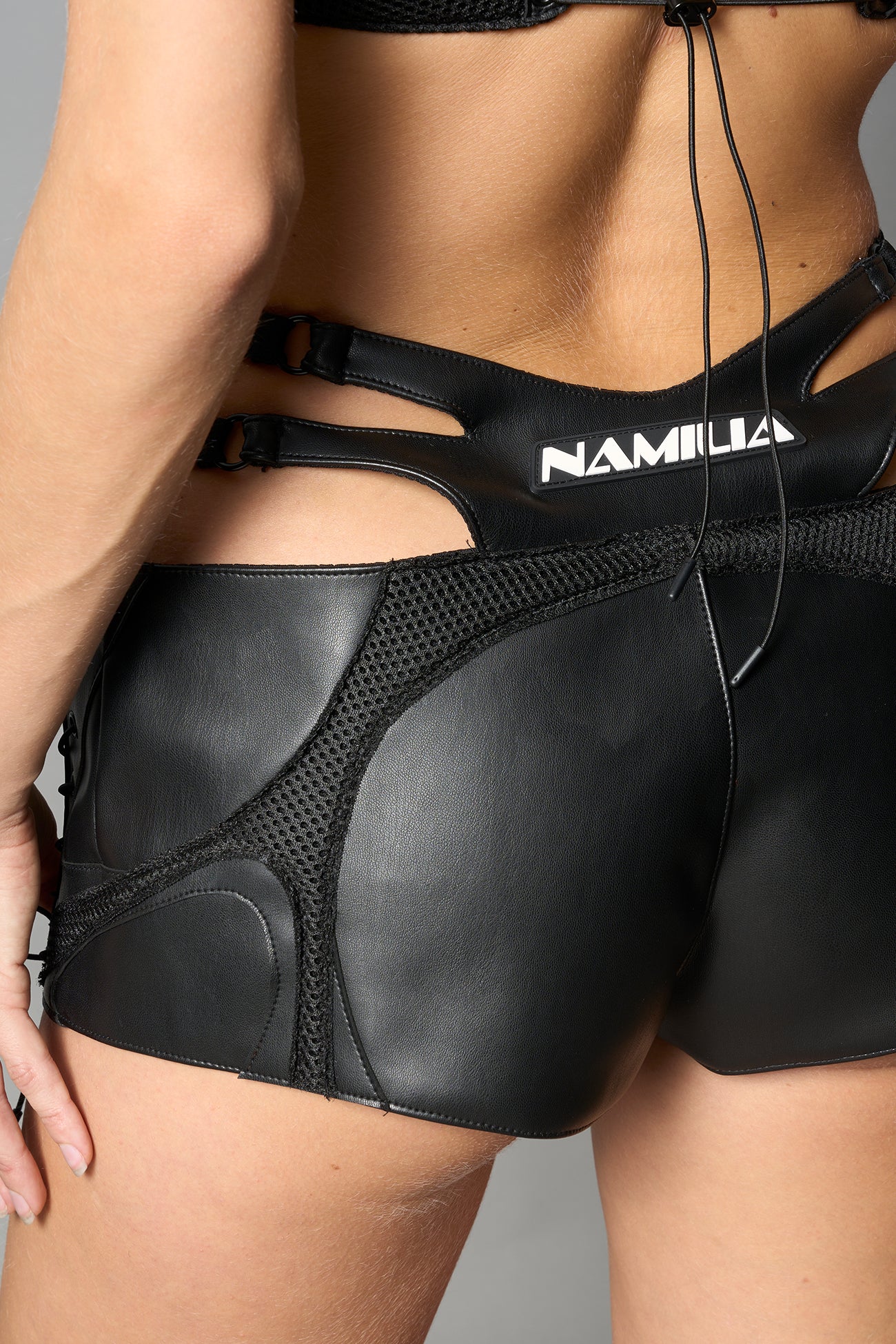 Black vegan leather sneaker-inspired hot pants with lace-up sides, cut-out hips, and front zip – edgy Y2K shorts for festival or streetwear looks.
