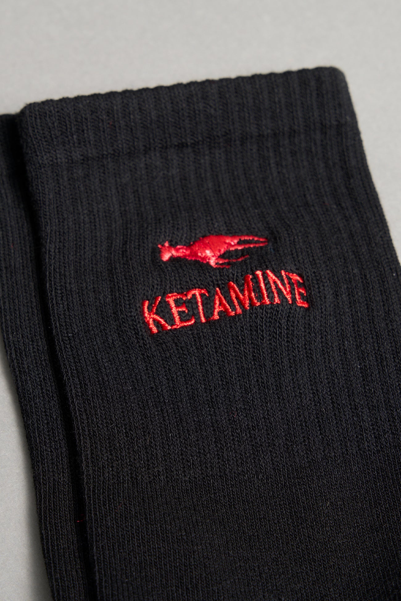 Black ribbed sport socks with red embroidered dragon and bold ‘KETAMINE’ slogan by Namilia, unisex mid-calf fit.