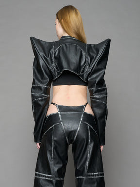 Model wearing a black vegan leather spike shoulder bolero jacket with cut-out design on a gray background