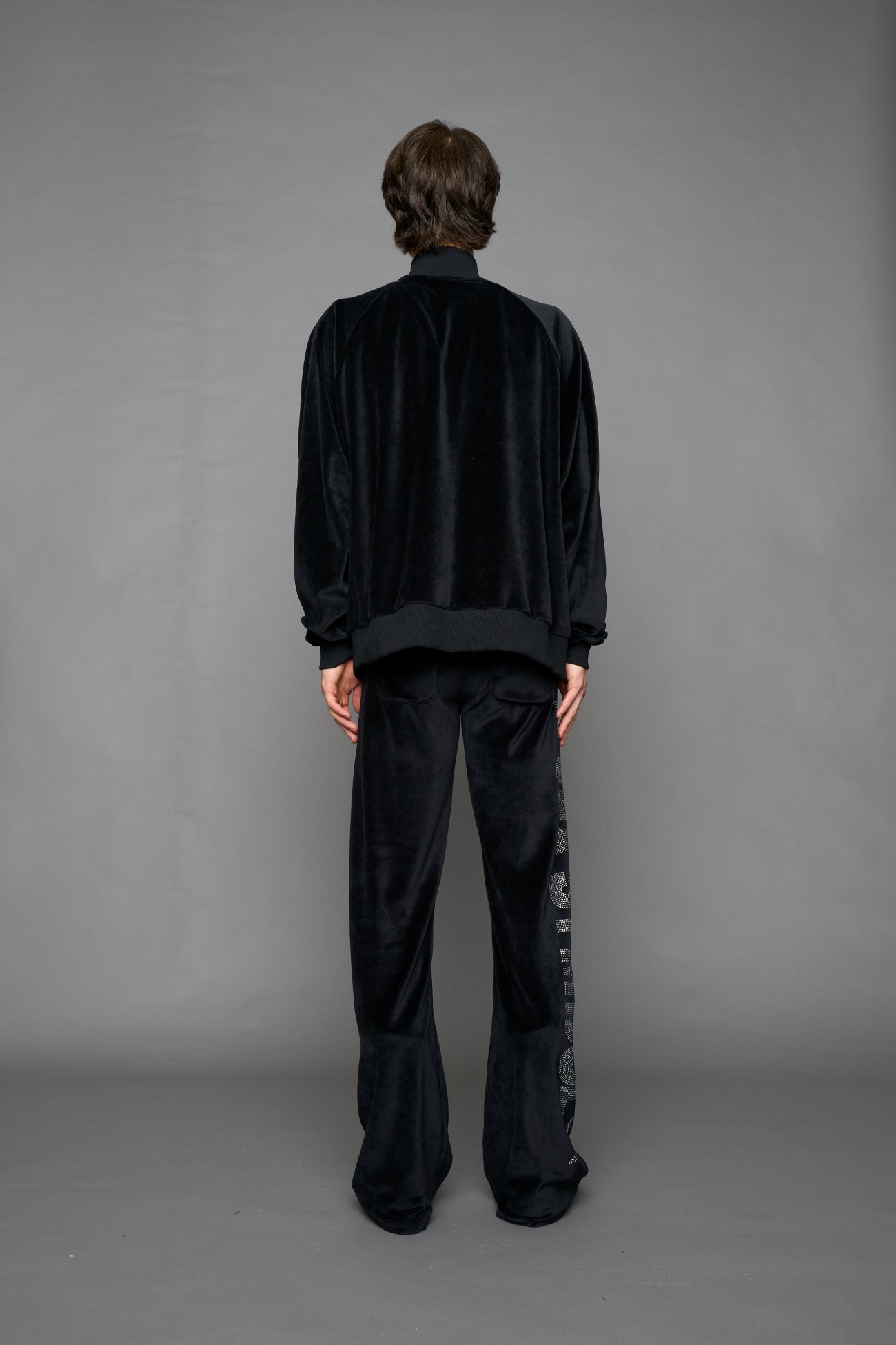 Person wearing a black velour jacket with 'S*X SYMBOL' crystal slogan on a gray background