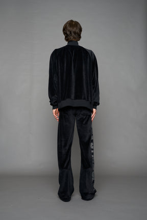 Person wearing a black velour jacket with 'S*X SYMBOL' crystal slogan on a gray background