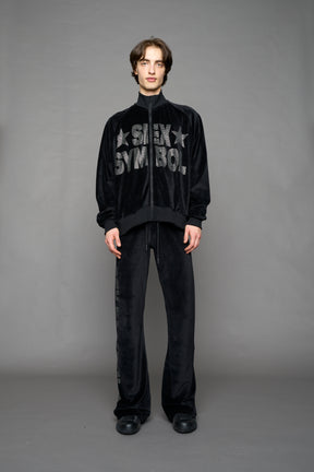 Person wearing a black velour jacket with 'S*X SYMBOL' crystal slogan on a gray background