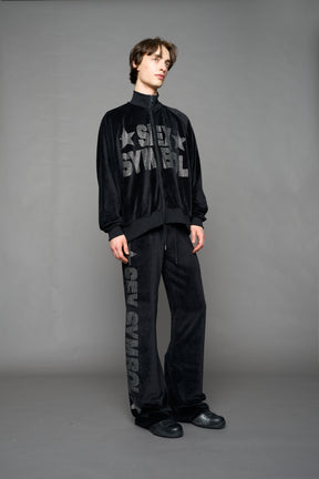 Person wearing a black velour jacket with 'S*X SYMBOL' crystal slogan on a gray background