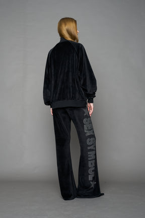 Person wearing a black velour jacket with 'S*X SYMBOL' crystal slogan on a gray background