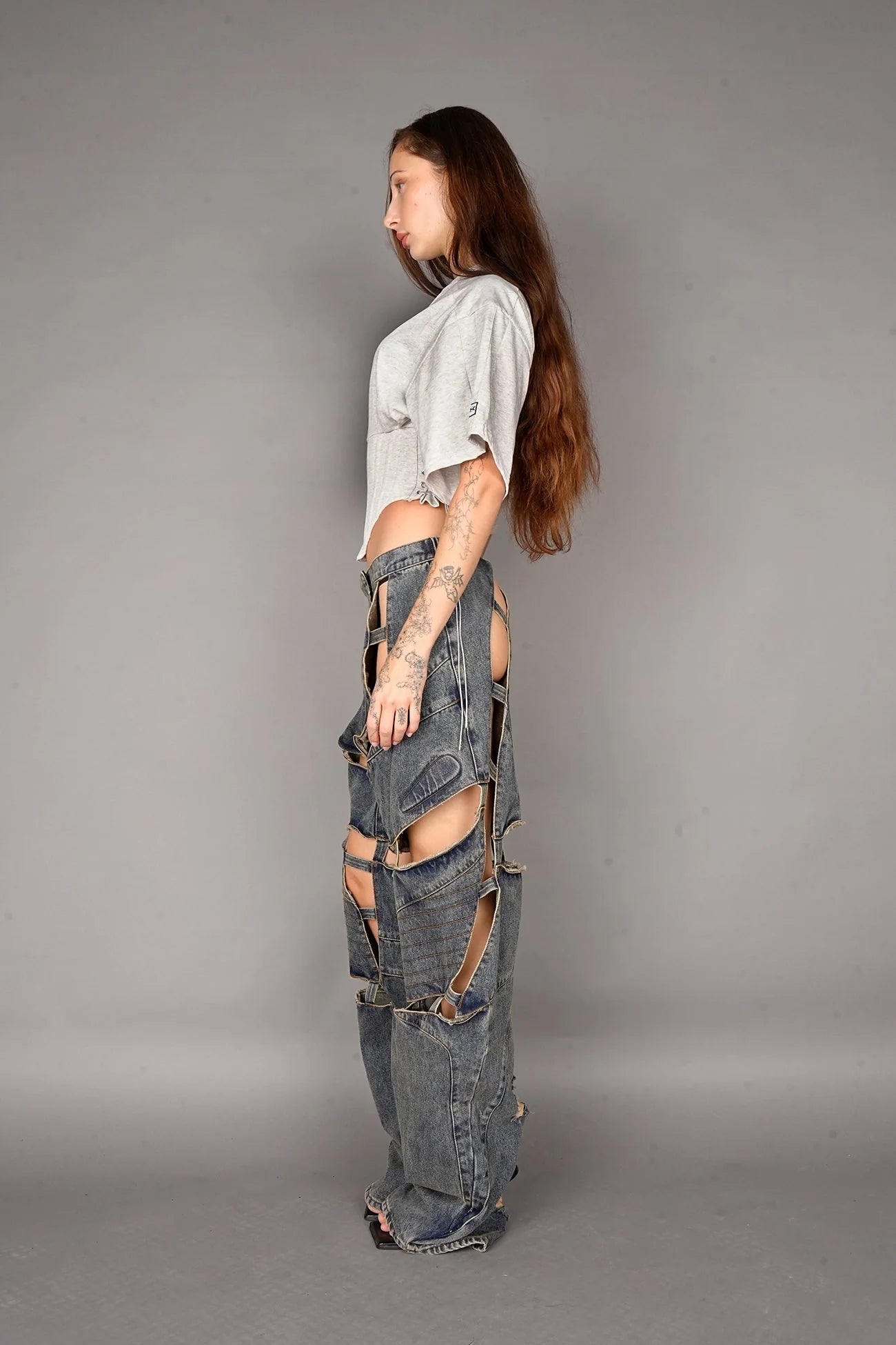 Person wearing a grey crop top and ripped jeans on a gray background