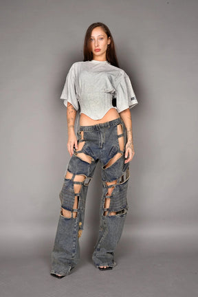 Person wearing a grey crop top and ripped jeans on a gray background