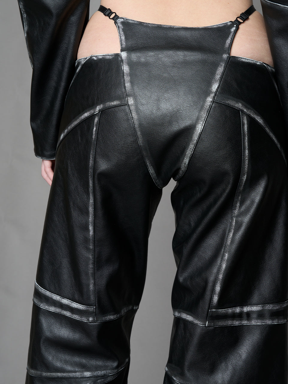 Person wearing a black thong pants with wide-legs and a jacket on a gray background