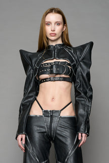 Model wearing a black vegan leather spike shoulder bolero jacket with cut-out design on a gray background