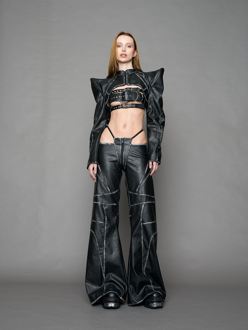 Person wearing a black thong pants with wide-legs and a jacket on a gray background