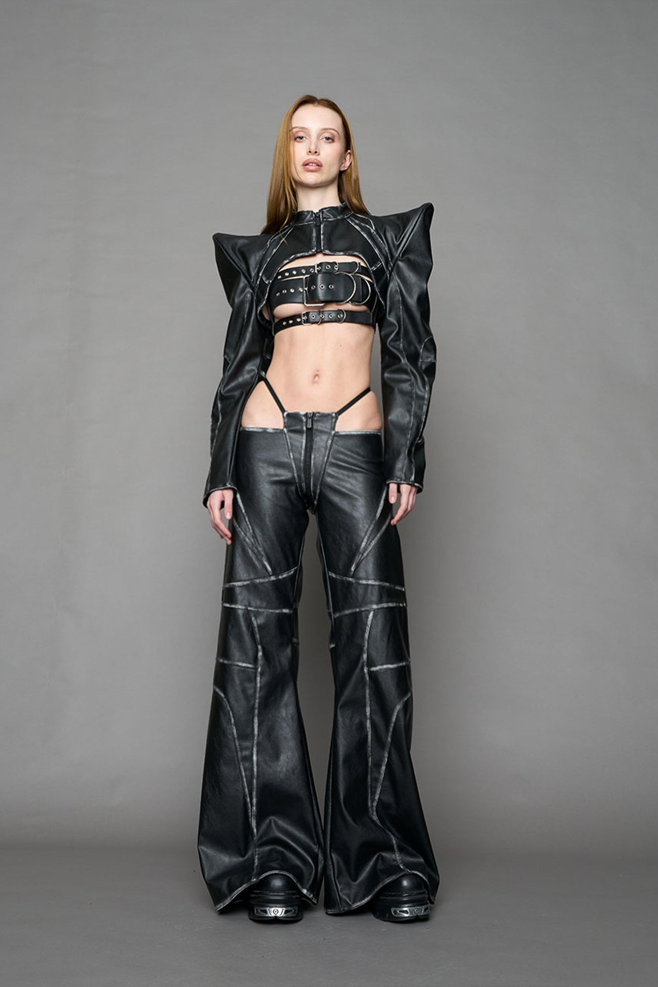 Person wearing a black thong pants with wide-legs and a jacket on a gray background