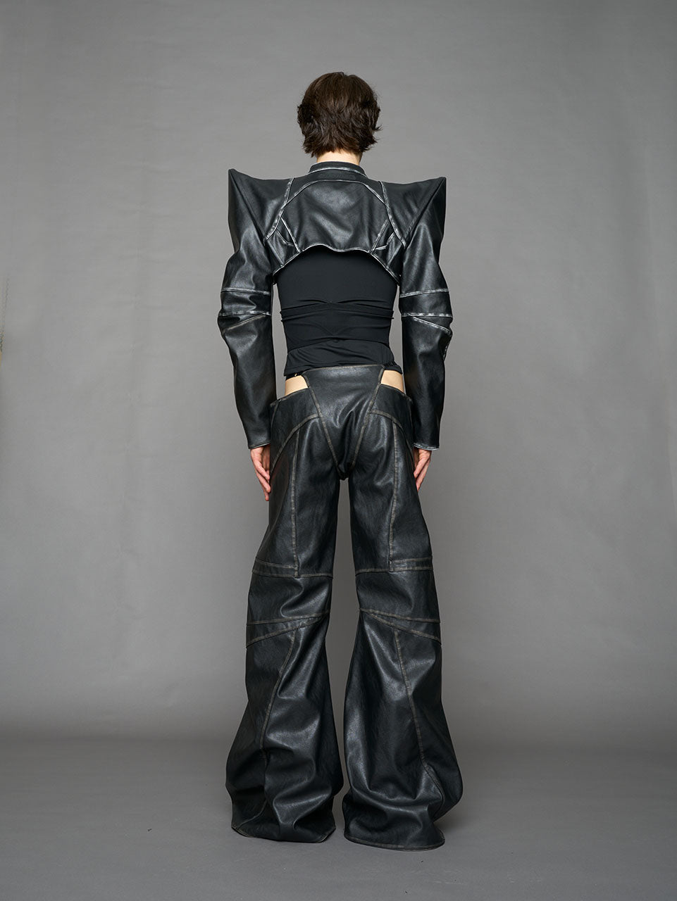 Person wearing a black thong pants with wide-legs and a jacket on a gray background