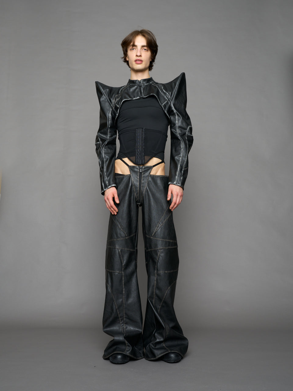 Model wearing a black vegan leather spike shoulder bolero jacket with cut-out design on a gray background