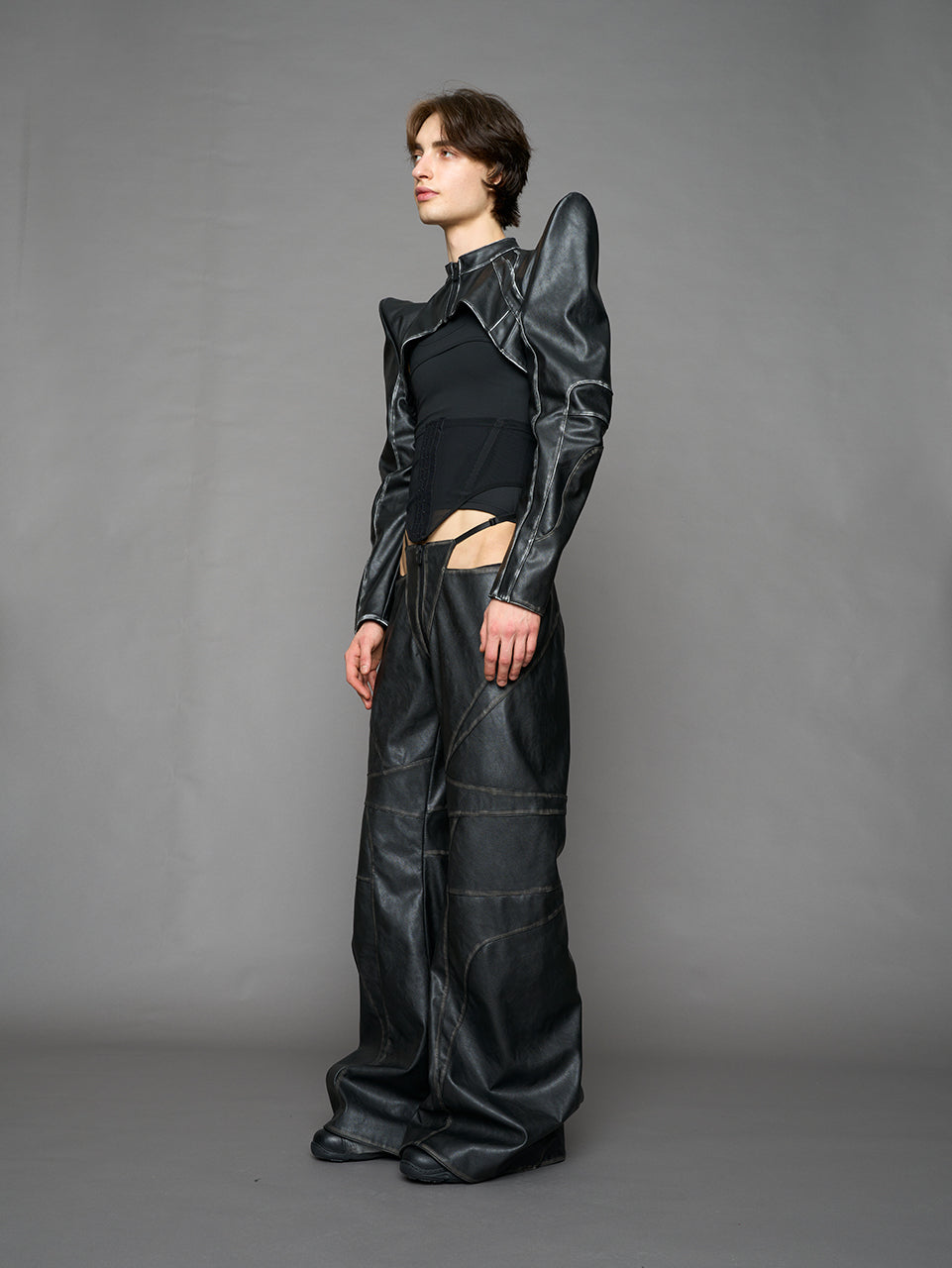 Person wearing a black thong pants with wide-legs and a jacket on a gray background