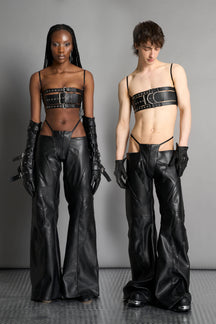 Low-rise flared pants in black faux leather with bold side cut-outs and thong strap detailing. Featuring moto-style paneling, front zip closure, and a sculpted fit. A statement piece for rave, nightlife, and runway-inspired looks.
