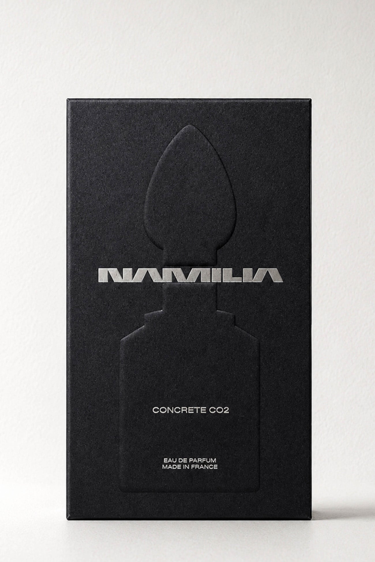 A bottle of Namilia Concrete CO2 Eau de Parfum with a large reflective black plug-shaped cap