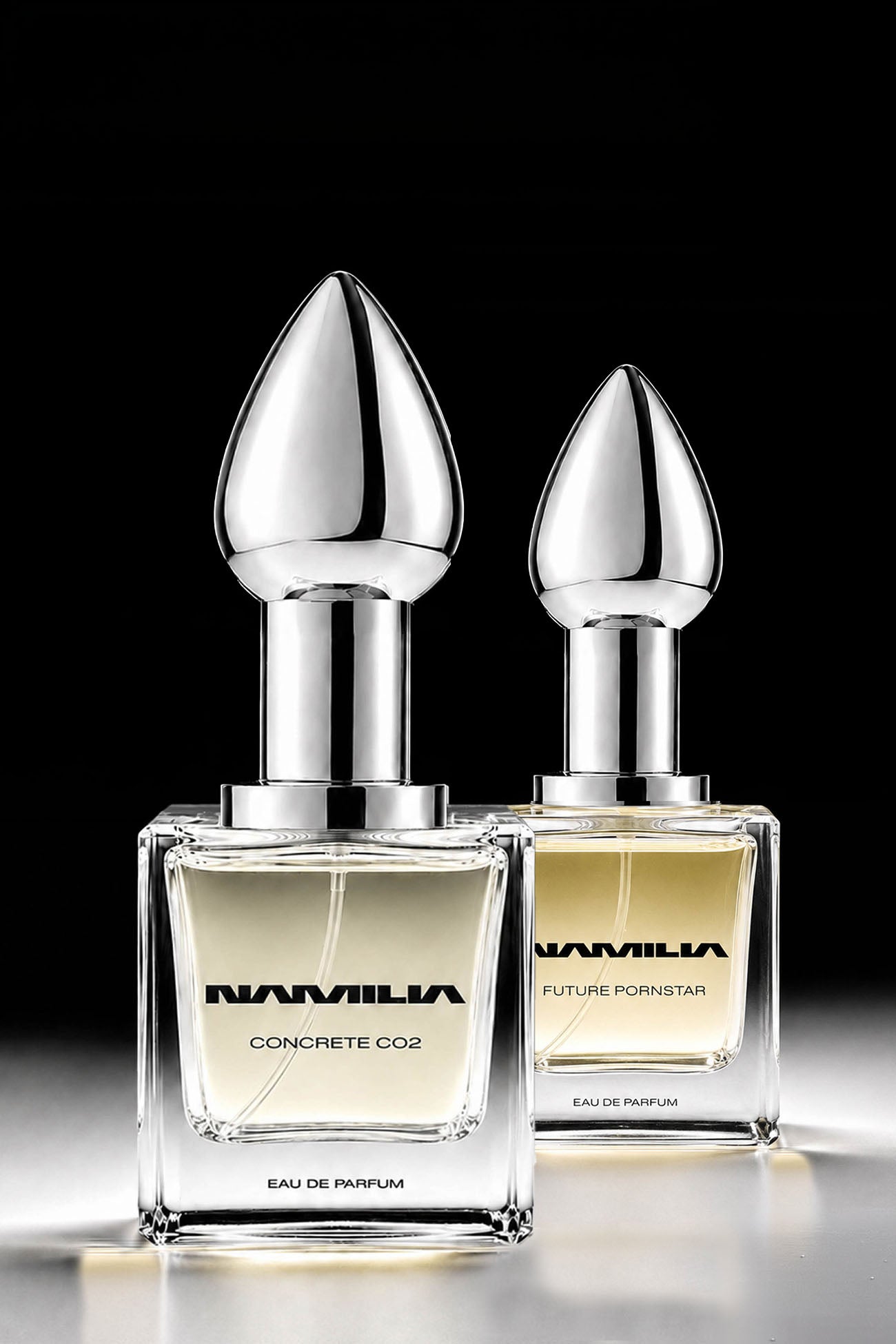 Two Namila perfume bottles with metallic silver shaped caps and clear glass bases, filled with pale yellow liquid