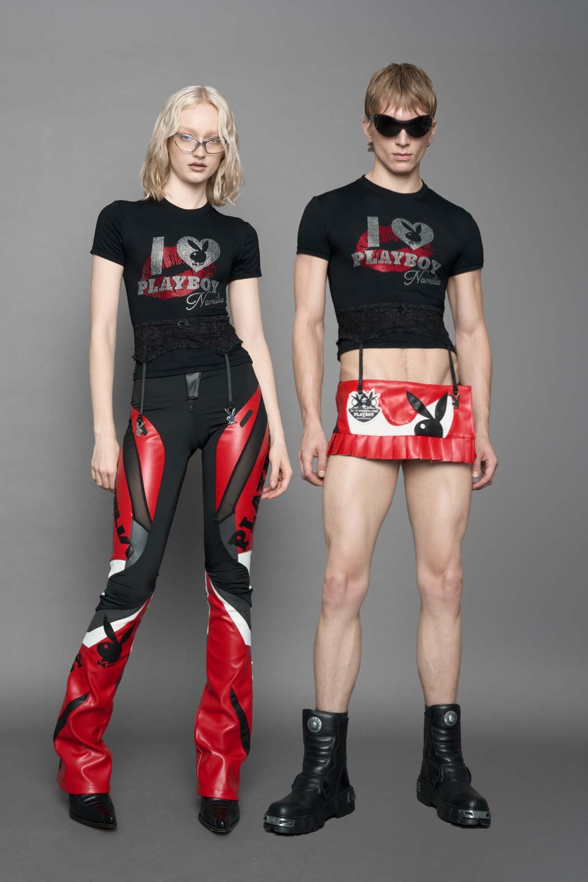 model wearing a black short-sleeve graphic t-shirt with rhinestone embroidery of red lip print and silver 'I <heart> PLAYBOY' design. T-Shirt has a lingerie black lace garter with suspender with metal silver Bunny Heads attached.
