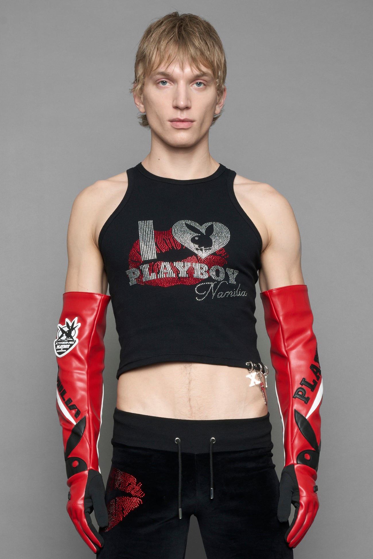 A model wearing a black halter crop top with red and silver 'I <heart> PLAYBOY Namilia' graphic, paired with black pants featuring a red lip print