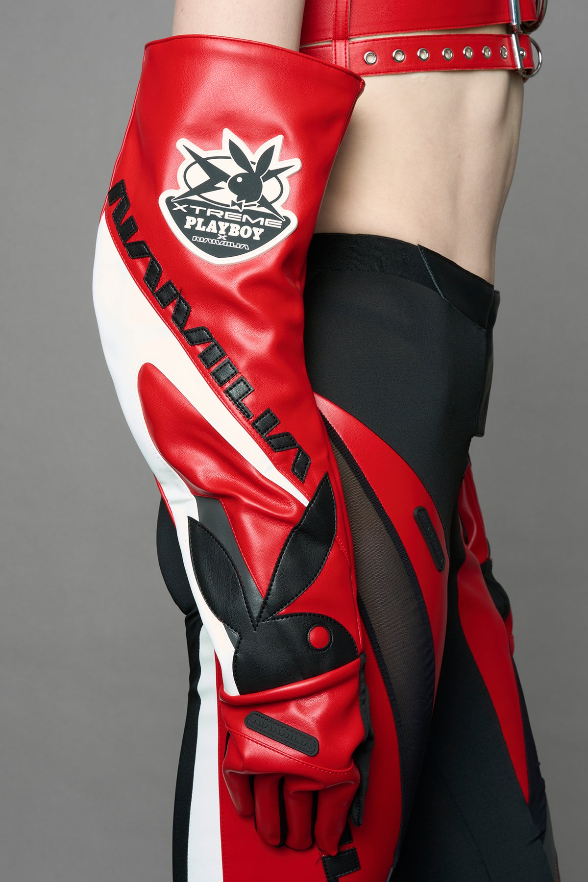 A model wears long motocross inspired red vegan Leather gloves with white and grey style paneling and black PU Leather 'Namilia' and 'Playboy' embroidery and a 'Playboy x Namilia' Rubbertag.