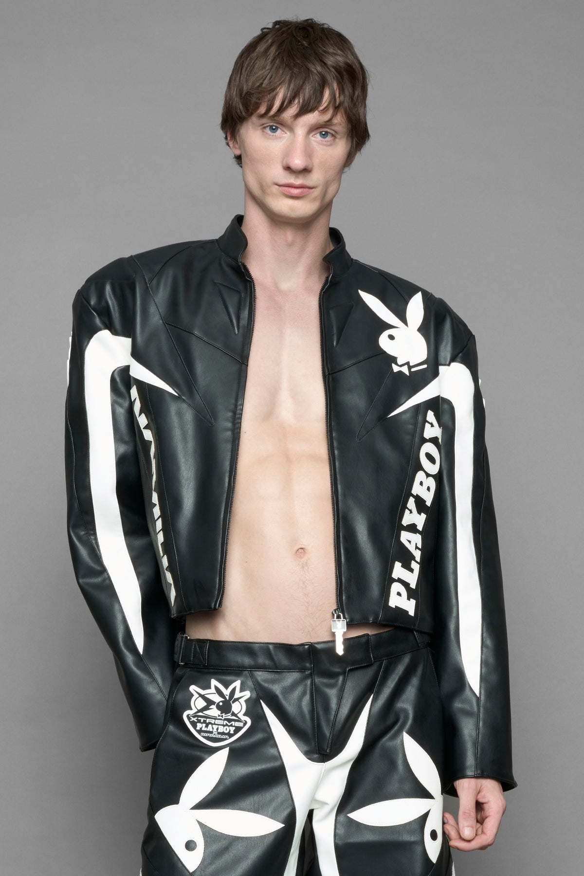 model wearing black vegan leather zip-up jacket with white PU leather 'Namilia' and 'Playboy' embroidery and black and white paneling. On the left chest there is a white Playboy Bunny Embroidery.