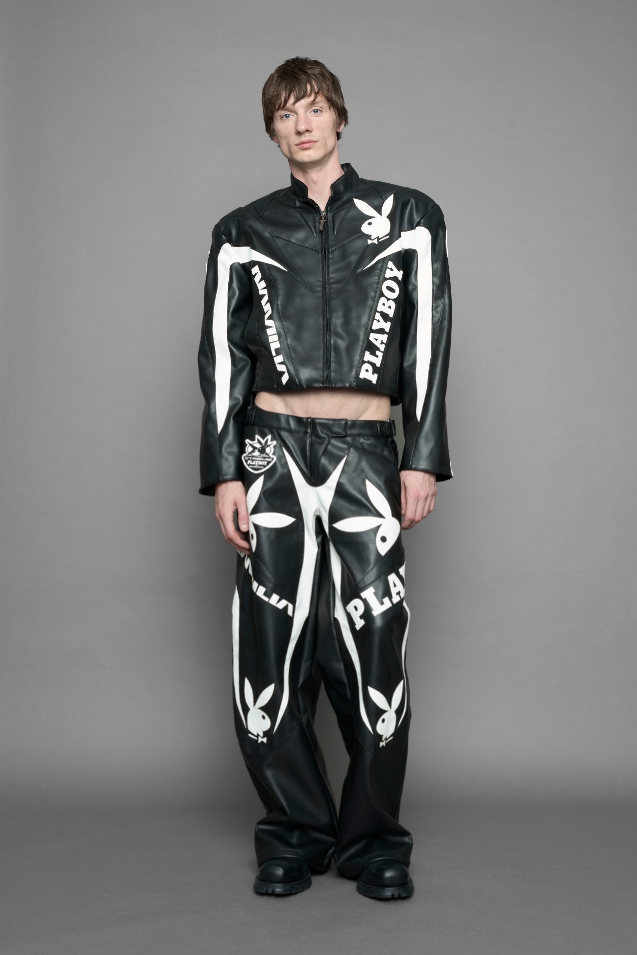 model wearing black vegan leather zip-up jacket with white PU leather 'Namilia' and 'Playboy' embroidery and black and white paneling. On the left chest there is a white Playboy Bunny Embroidery.