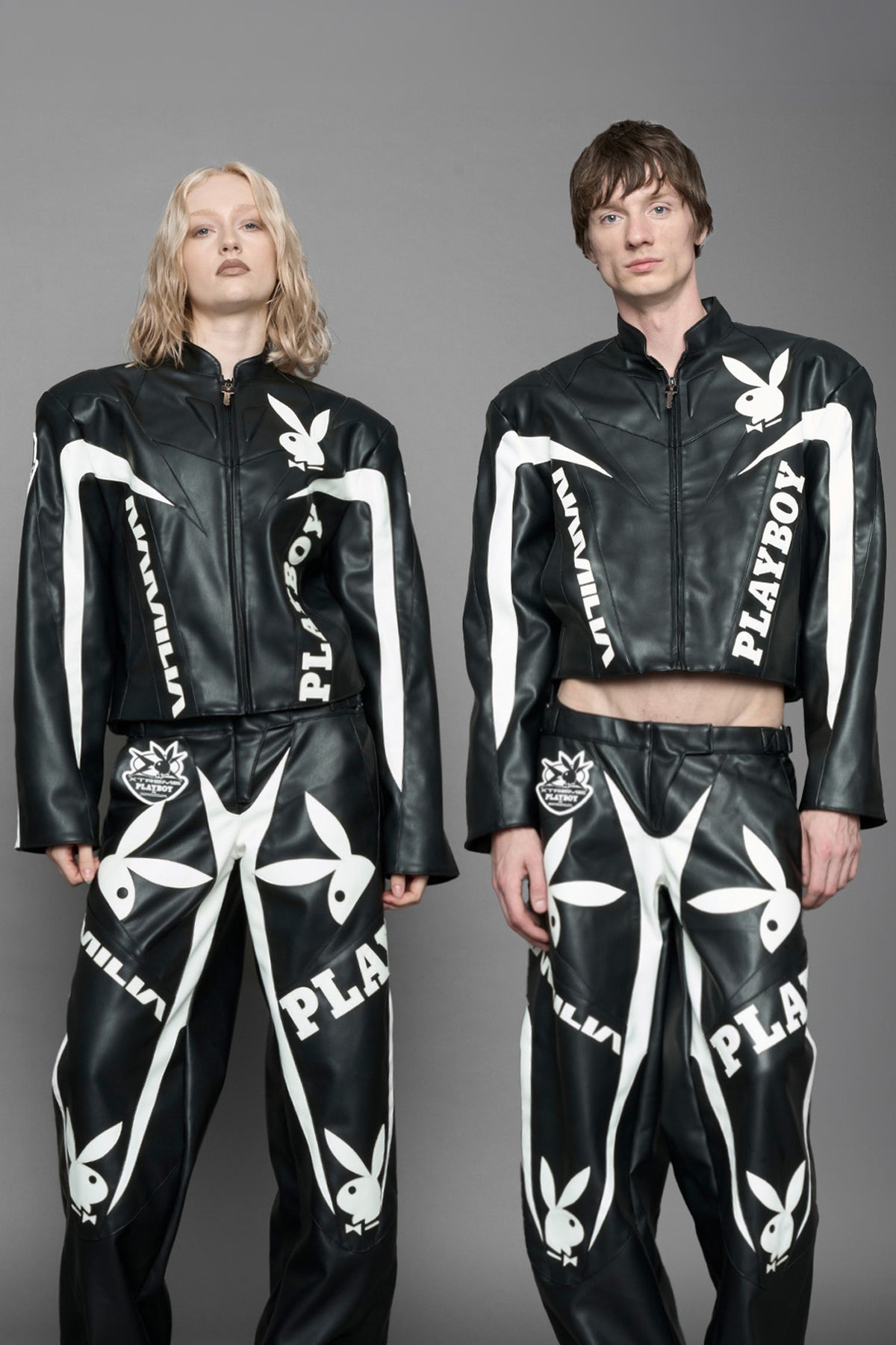 model wearing black vegan leather zip-up jacket with white PU leather 'Namilia' and 'Playboy' embroidery and black and white paneling. On the left chest there is a white Playboy Bunny Embroidery.