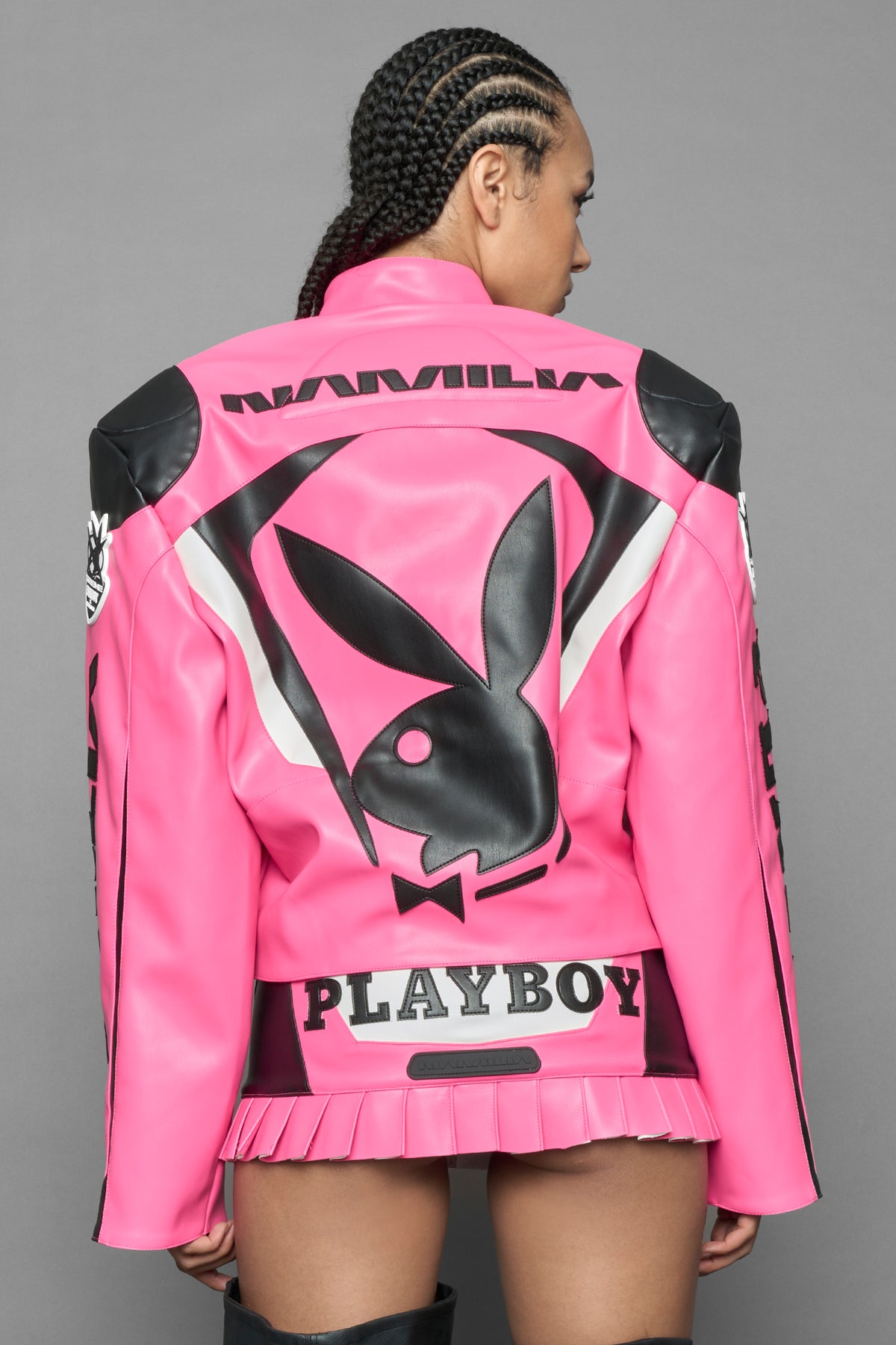 model wearing pink vegan leather zip-up jacket with black PU leather 'Namilia' and 'Playboy' embroidery and black and white paneling. On the left chest there is a white Playboy Bunny Embroidery.