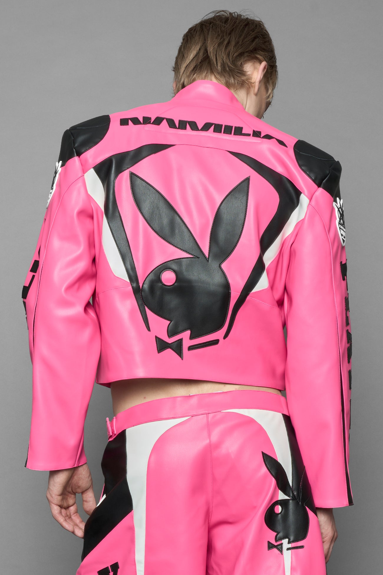 model wearing pink vegan leather zip-up jacket with black PU leather 'Namilia' and 'Playboy' embroidery and black and white paneling. On the left chest there is a white Playboy Bunny Embroidery.