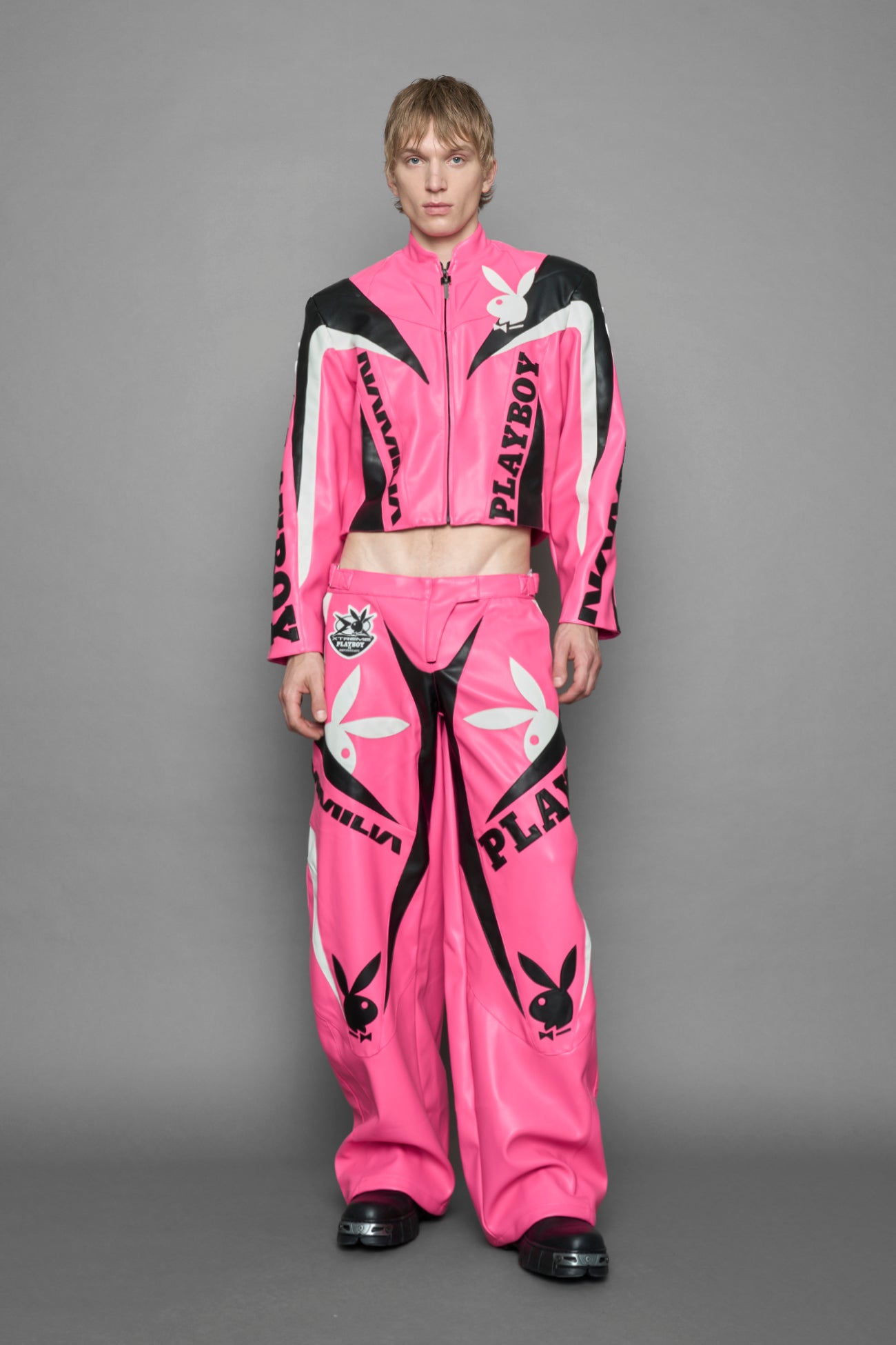 model wearing pink vegan leather zip-up jacket with black PU leather 'Namilia' and 'Playboy' embroidery and black and white paneling. On the left chest there is a white Playboy Bunny Embroidery.