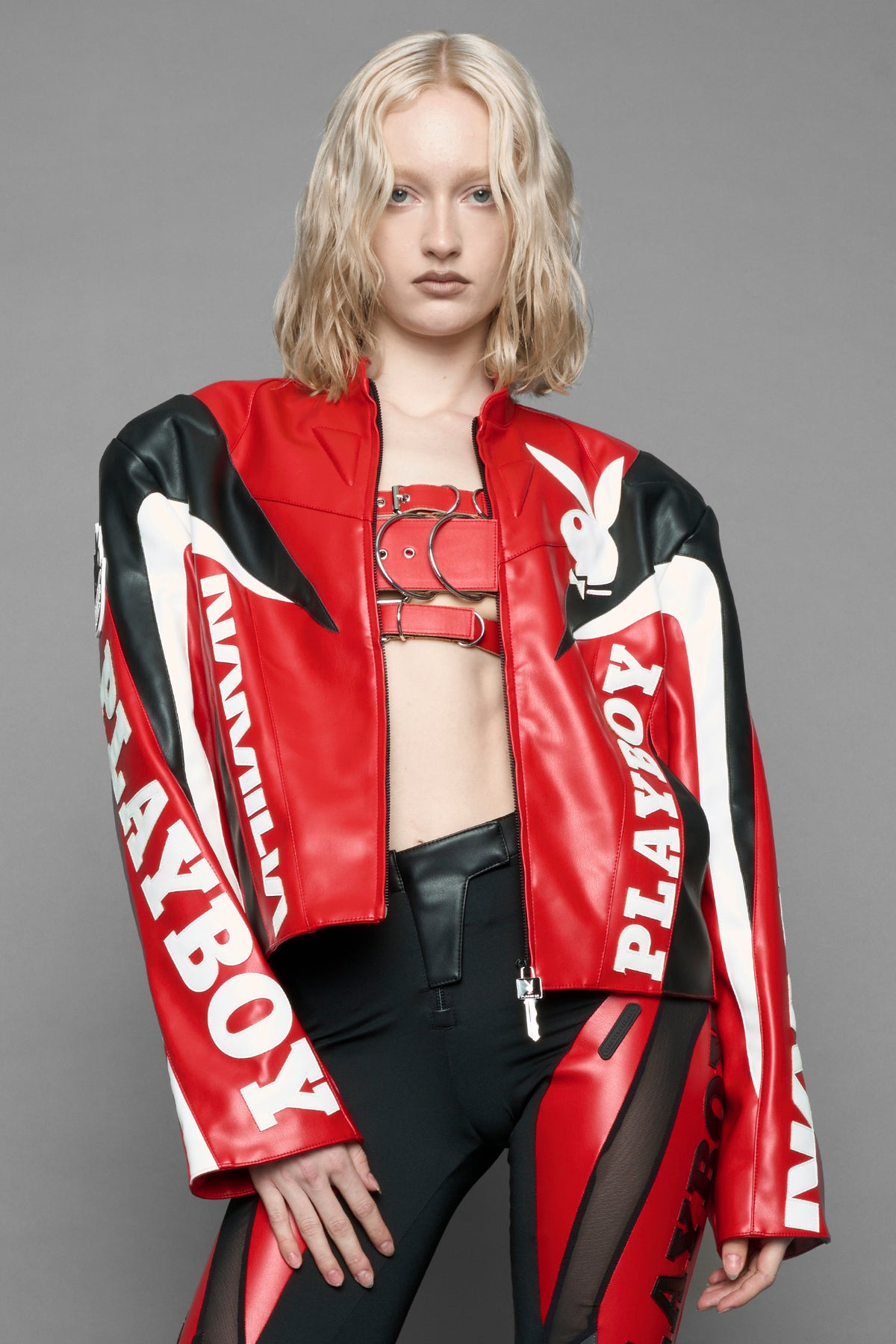 model wearing red vegan leather zip-up jacket with black PU leather 'Namilia' and 'Playboy' embroidery and black and white paneling. On the left chest there is a white Playboy Bunny Embroidery.
