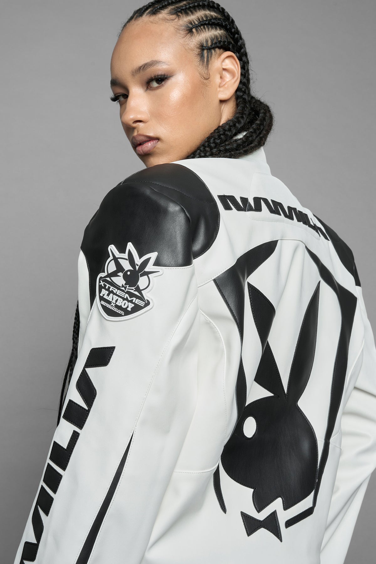 model wearing white vegan leather zip-up jacket with black PU leather 'Namilia' and 'Playboy' embroidery and black and white paneling. On the left chest there is a white Playboy Bunny Embroidery.