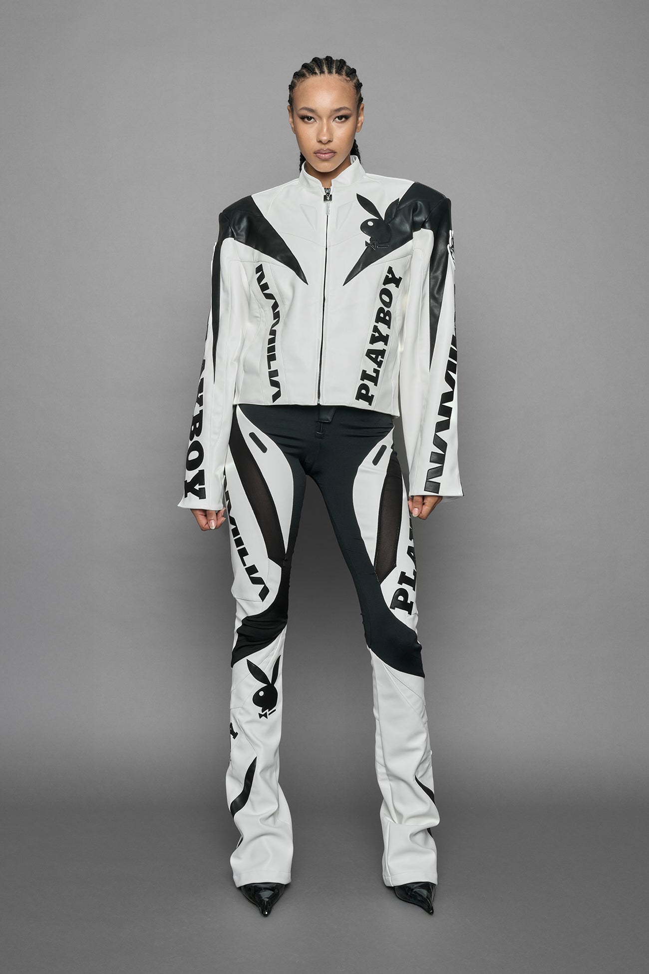 model wearing white vegan leather zip-up jacket with black PU leather 'Namilia' and 'Playboy' embroidery and black and white paneling. On the left chest there is a white Playboy Bunny Embroidery.