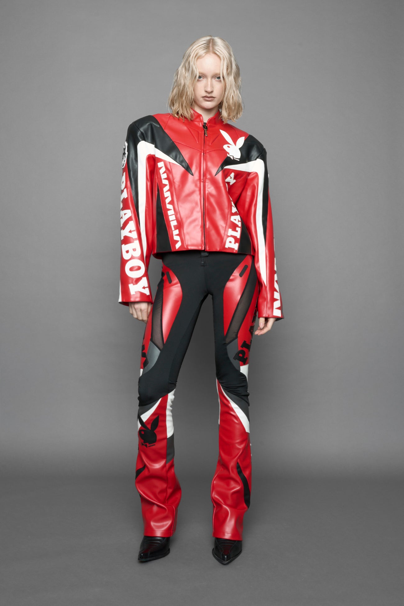 model wearing red vegan leather zip-up jacket with black PU leather 'Namilia' and 'Playboy' embroidery and black and white paneling. On the left chest there is a white Playboy Bunny Embroidery.