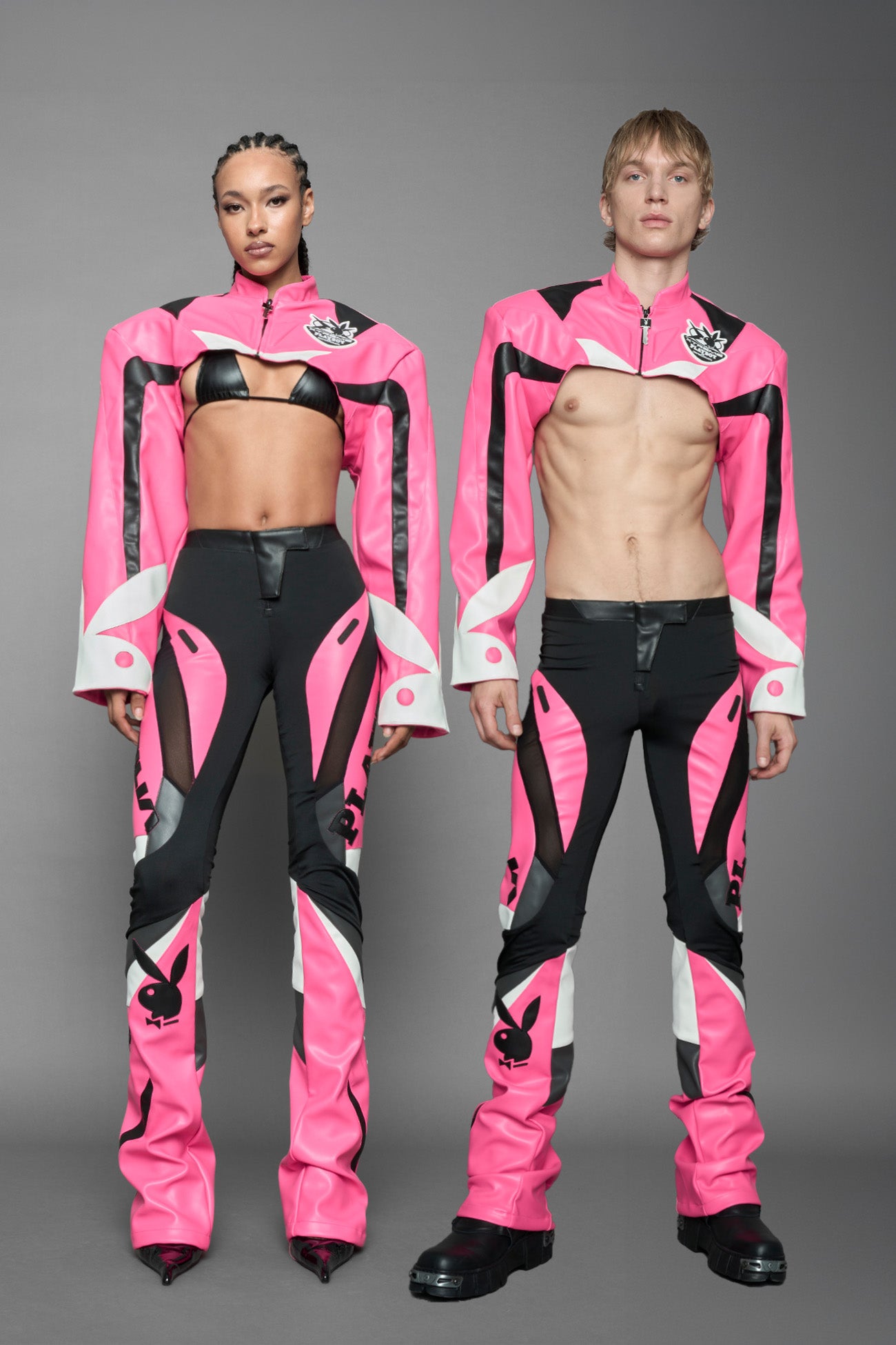 model wearing a vegan leather cropped jacket with broad shoulders in pink with black and white paneling. The jacket has PU leather embroidery of 'Namilia' and 'Playboy' with a key formed zipper pull and a rubbertag on the left breast.