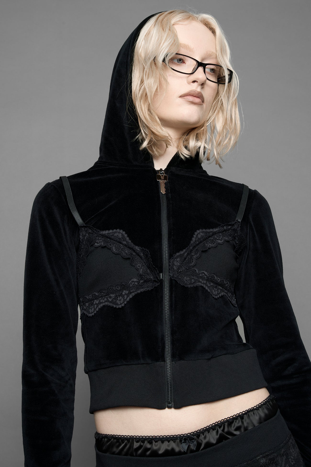 A female model is wearing a black velvet cropped zip-up hoodie with a black lace bralette and a Playboy branded key formed Zipper Pull 